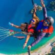 A woman and a man paragliding underneath of them a island of Ölüdeniz.