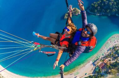 A woman and a man paragliding underneath of them a island of Ölüdeniz.