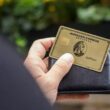 The American Express® Gold Card being held up in front of a bright blue wall