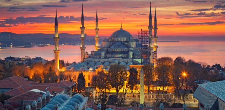 On a sunset atmosphere, an old mosque, surrounded by smaller building structures and a few trees.